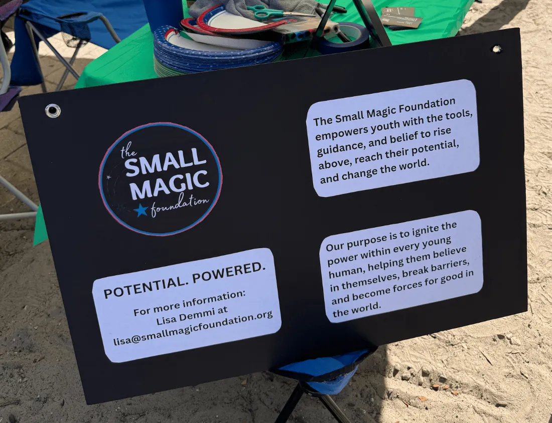 A black sign promoting The Small Magic Foundation on an event table