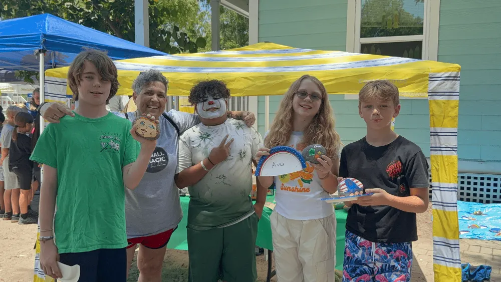 A group of five kids and an adult in clown makeup standing under a yellow and blue tent at an event